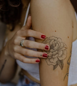 Person with a floral tattoo on their arm and red nail polish.
