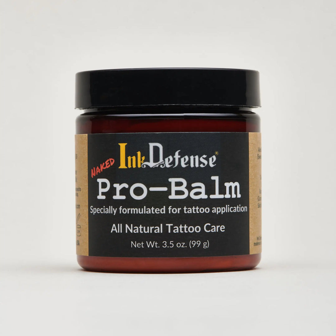 A dark amber glass jar with black lid and label of naked ink defense pro-balm all-natural tattoo care for artists