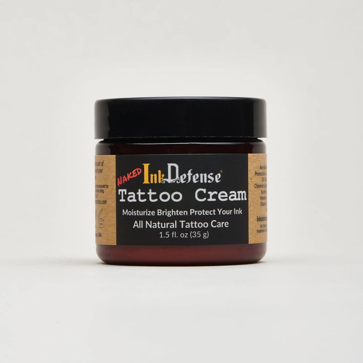A dark amber glass jar with black lid containing naked ink defense tattoo cream for tattoo aftercare
