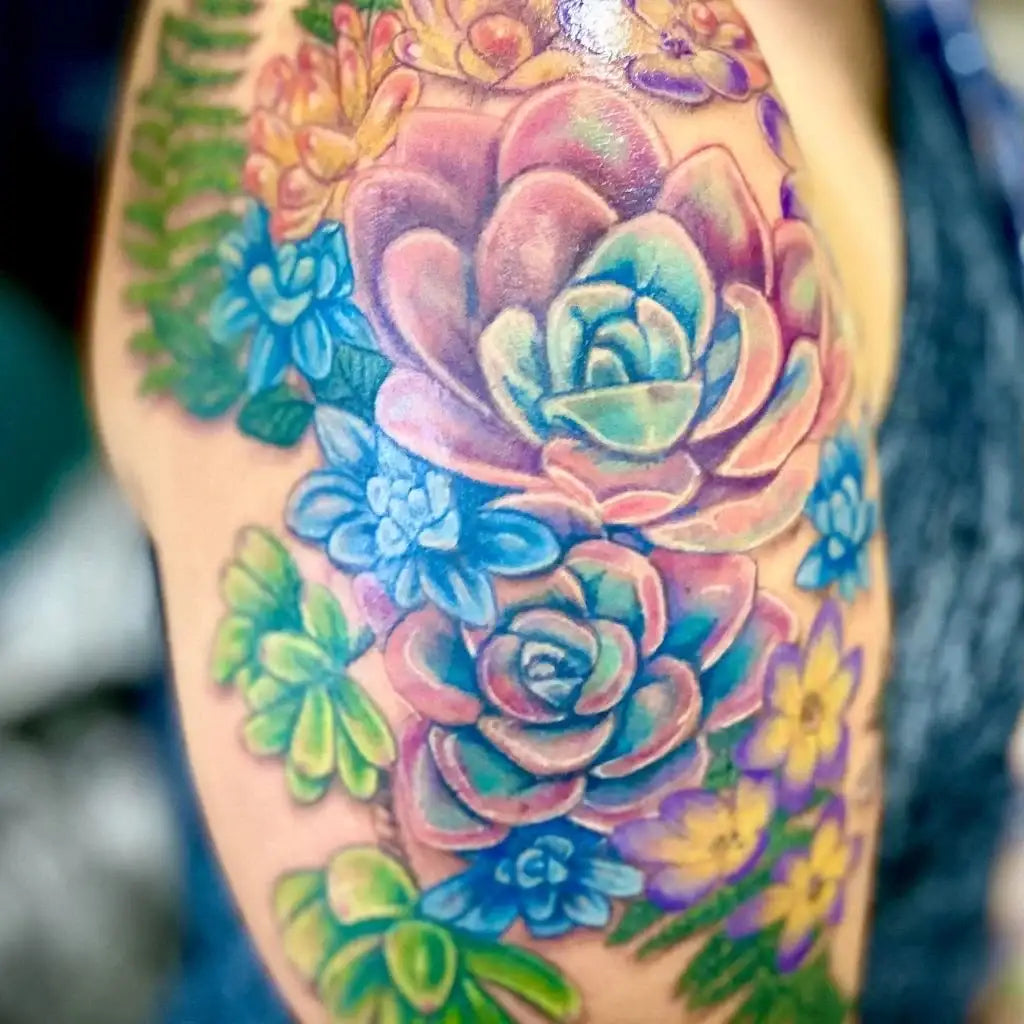 A vibrant, colorful tattoo of succulents and flowers in shades of pink, blue, green, and yellow on a person’s arm.